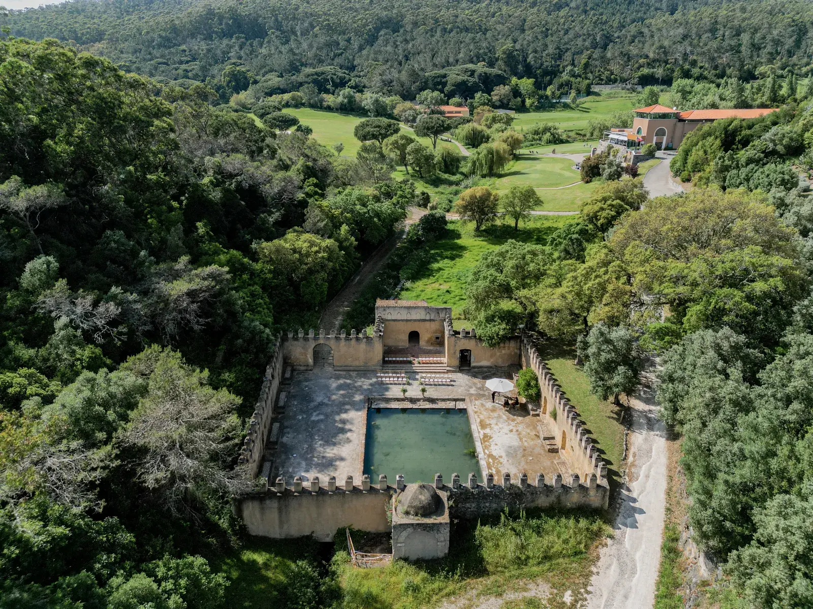 Drone view of a centuries-old crenellated water tank amid pine woods, its pool dark and still