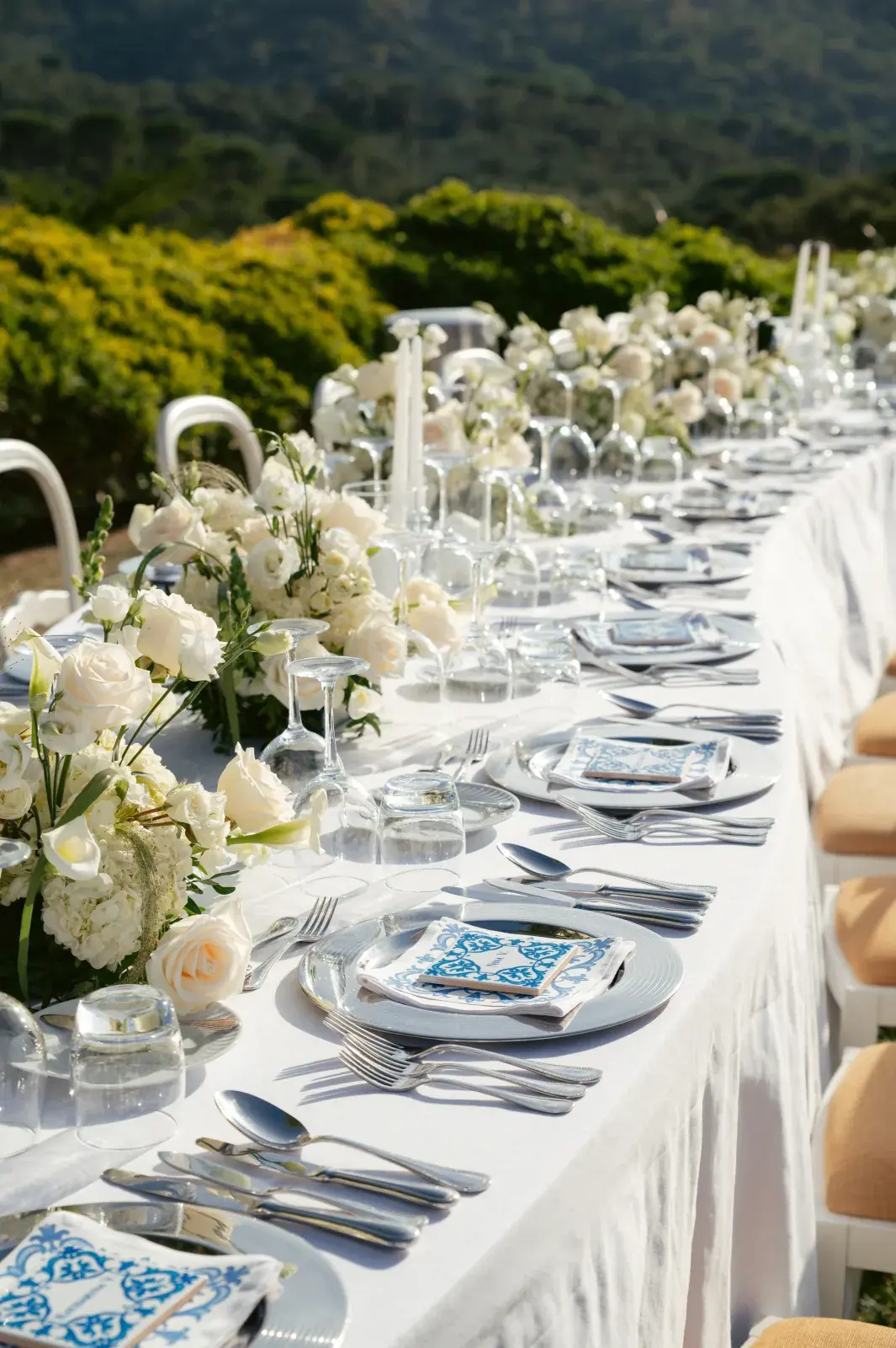 Long outdoor table with white flowers, glass cloches and azulejo-print menus, wooded hills beyond
