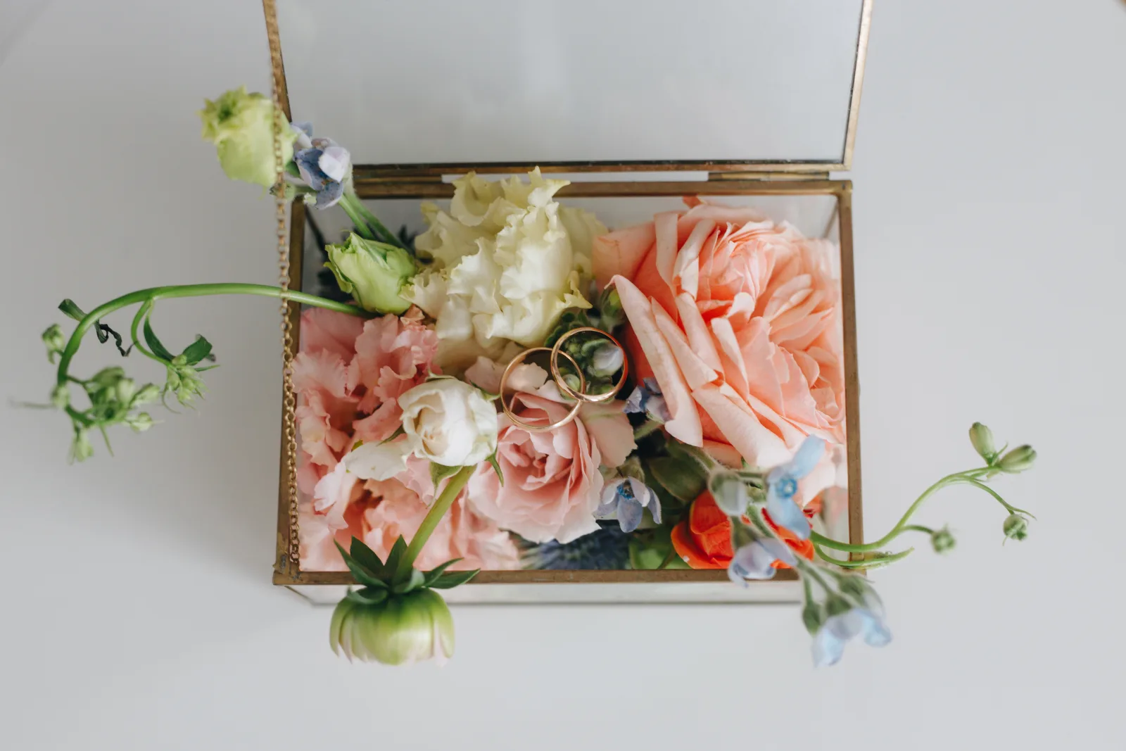 Glass ring box filled with peach and pink roses, the wedding bands nested among the petals