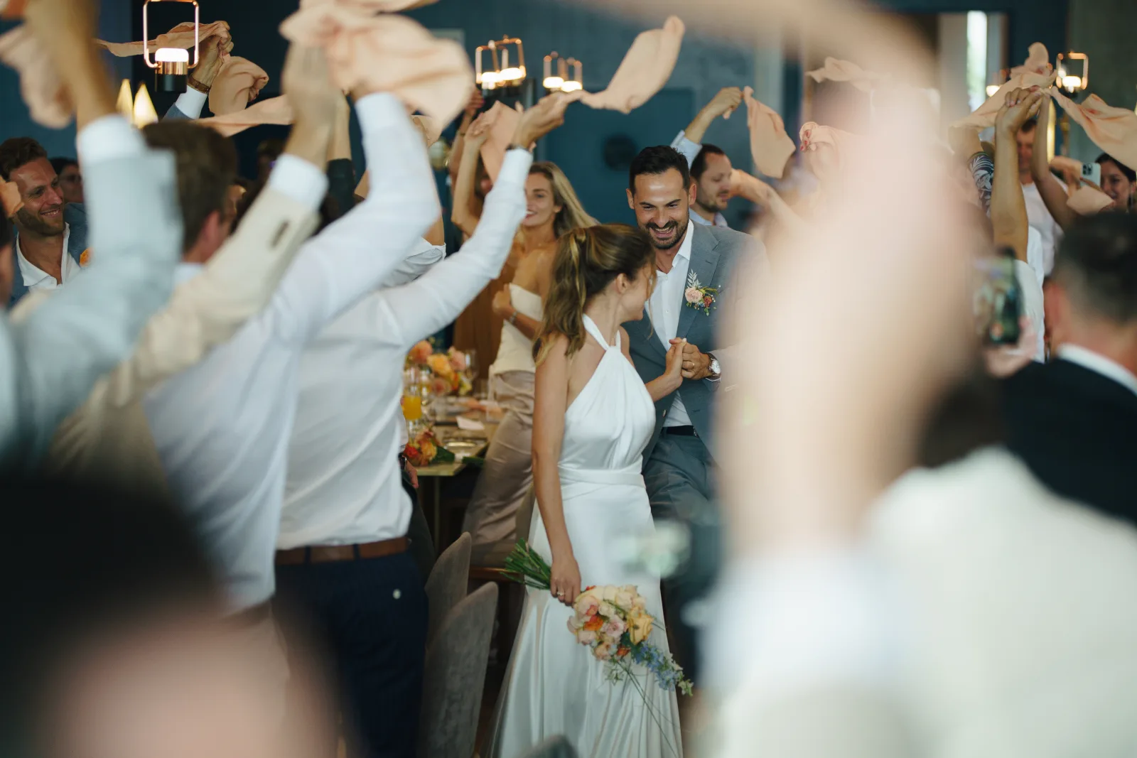 Guests waving napkins around the newlyweds at the reception dinner, the room mid-celebration
