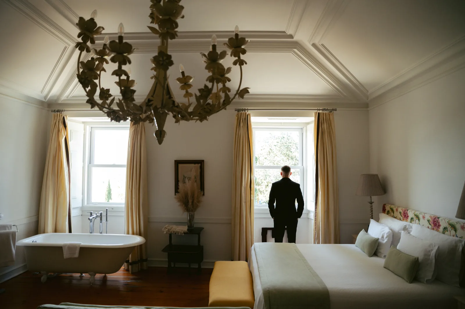 Manor suite with a claw-foot bath and wrought-iron chandelier, the groom waiting at the window