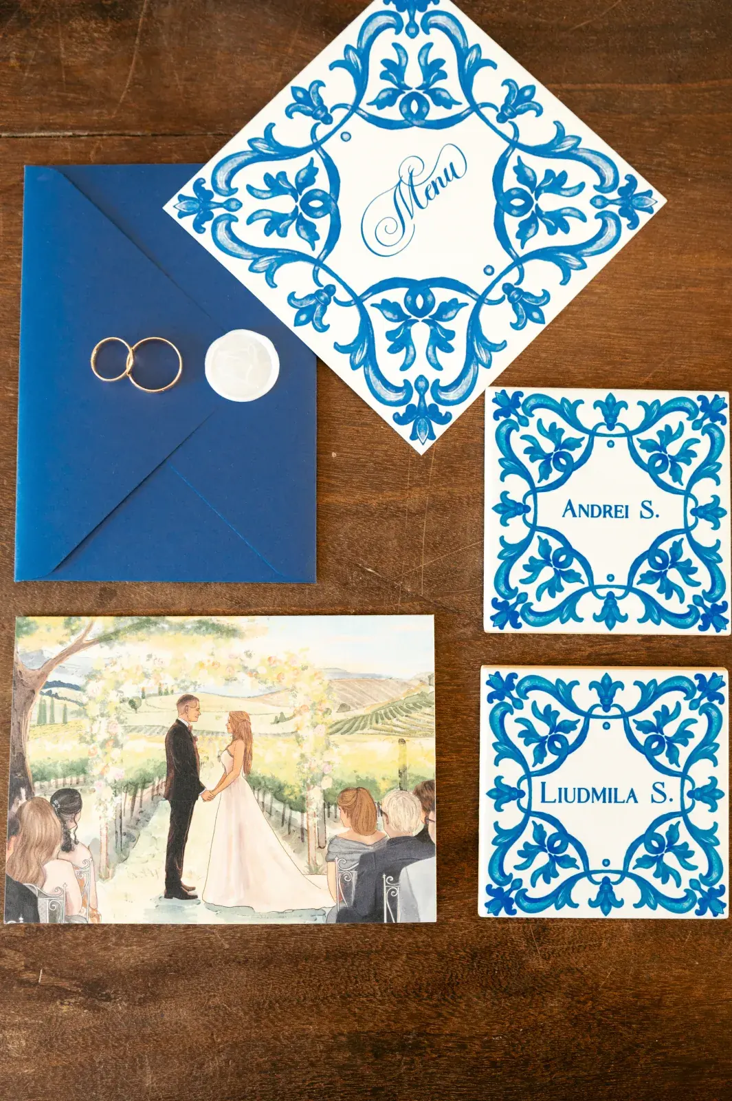 Stationery suite with azulejo-patterned place cards, navy envelope, rings and a painted vineyard scene