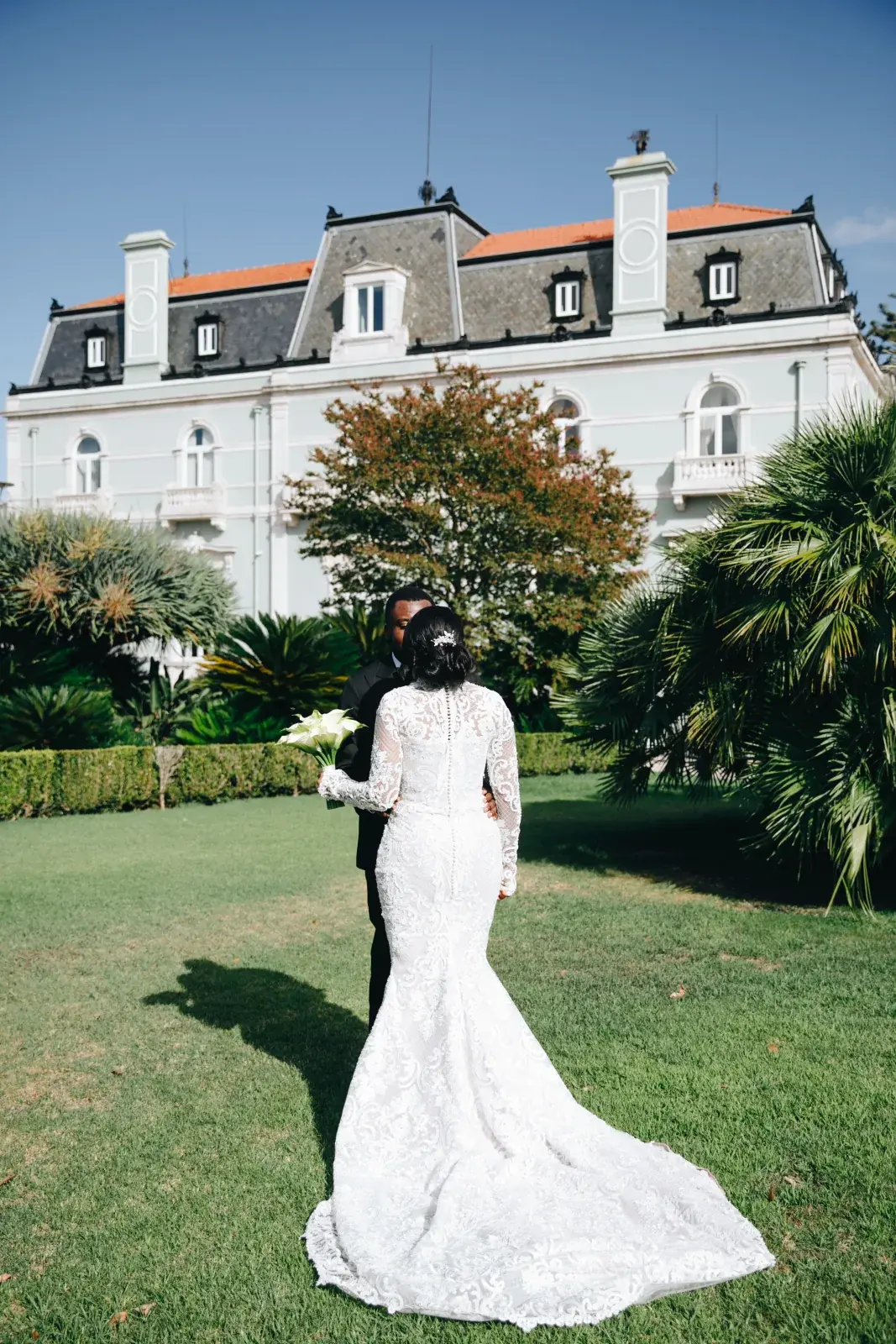 Bride in long-sleeved lace crossing the lawn toward a Belle Epoque palace facade