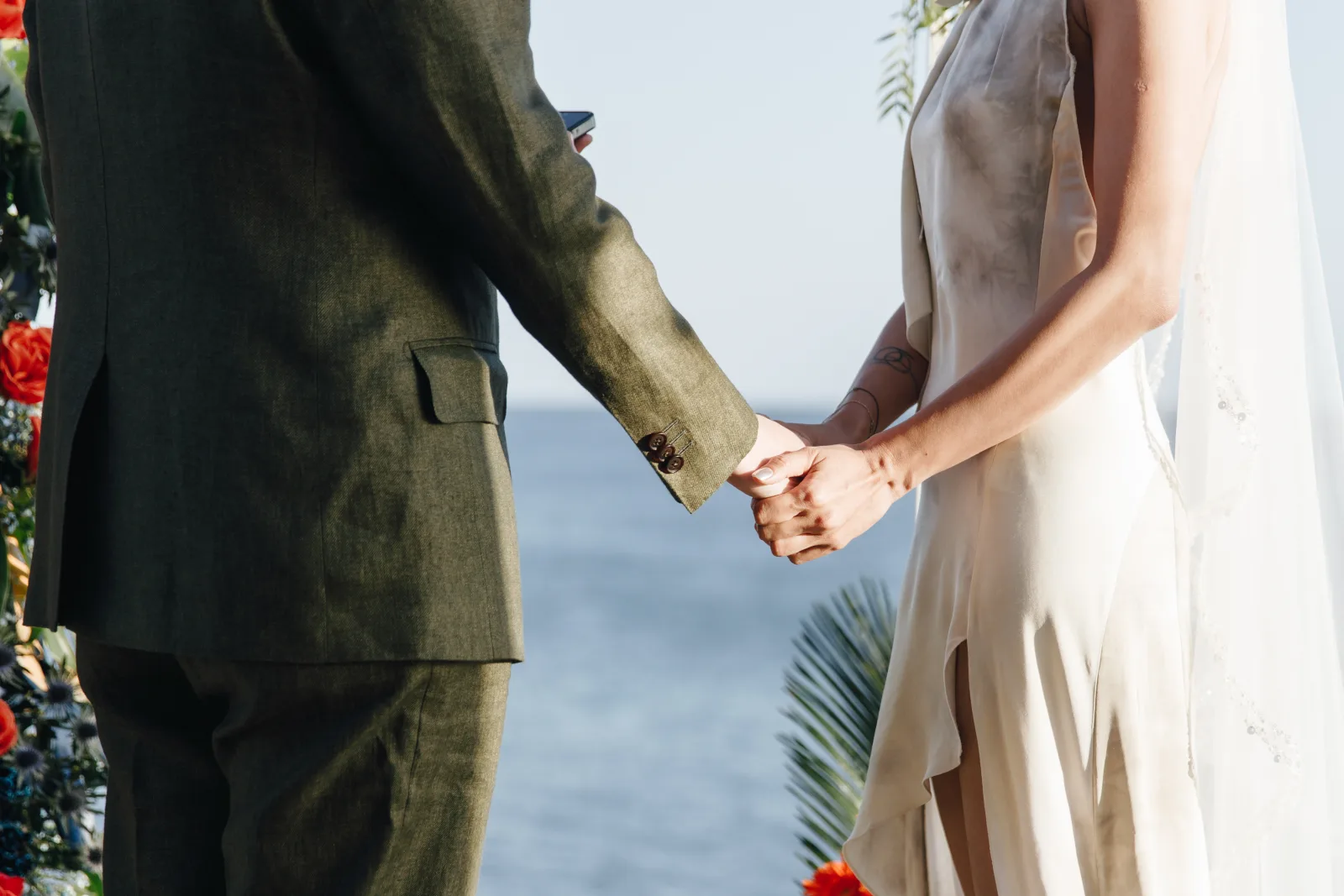 Bride and groom joining hands at a seaside ceremony, the Atlantic flat to the horizon behind them