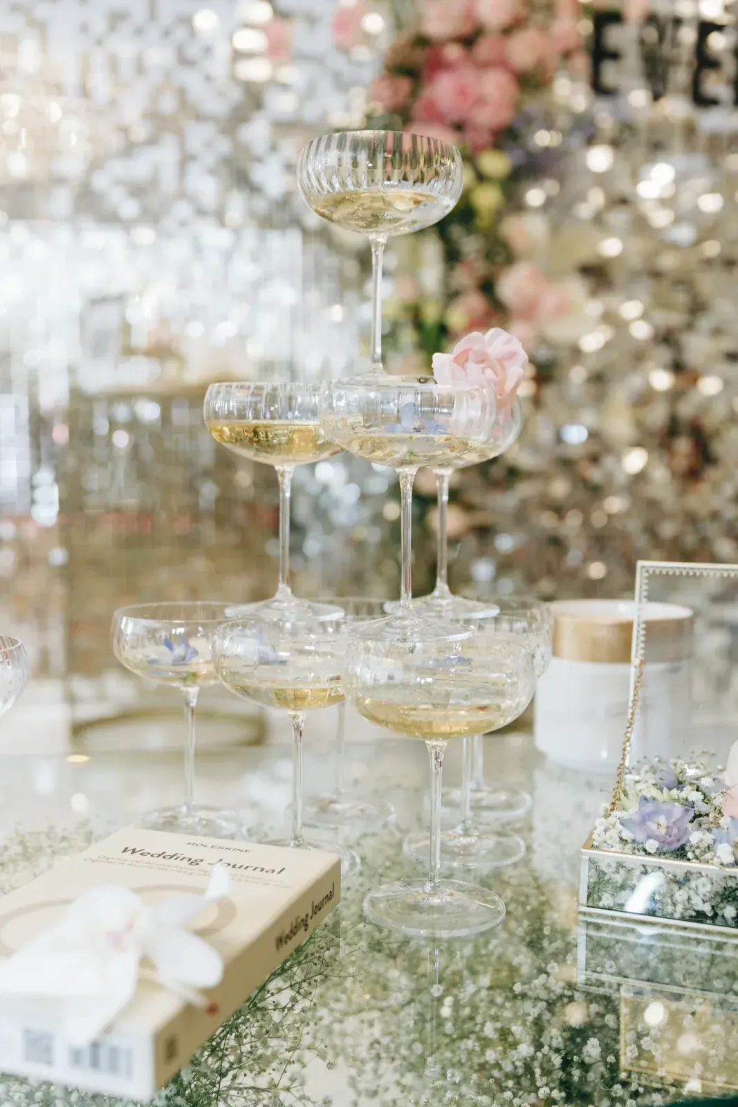 Champagne coupe tower on a mirrored table against a sequinned backdrop, an orchid to one side
