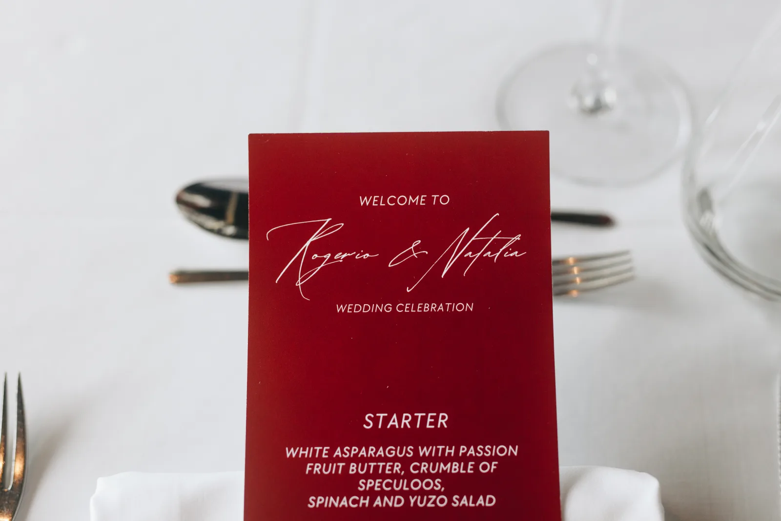 Claret-red printed welcome card and menu standing at a white place setting for the wedding dinner