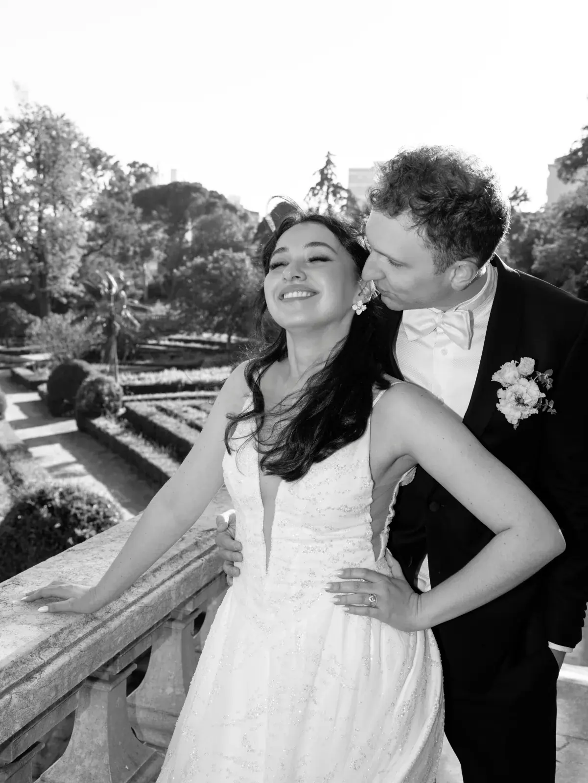 Groom kissing the bride's temple on a terrace above the parterre garden, in black and white