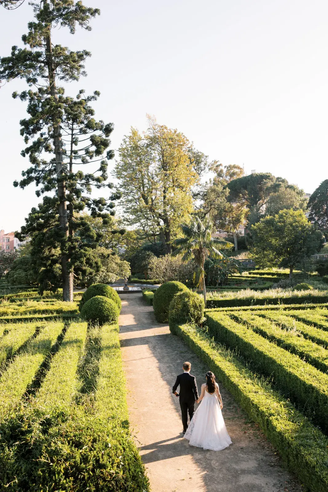 Couple walking hand in hand through clipped box parterres in a Lisbon palace garden