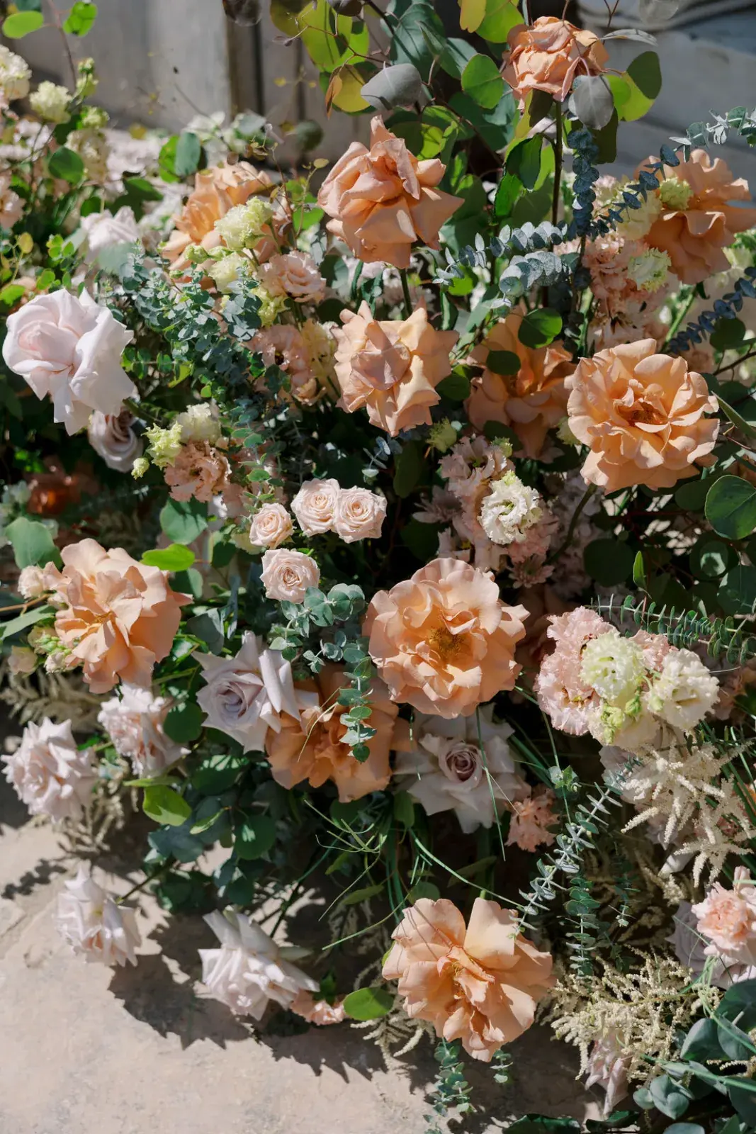 Arrangement of toffee, blush and cream roses with eucalyptus resting on stone