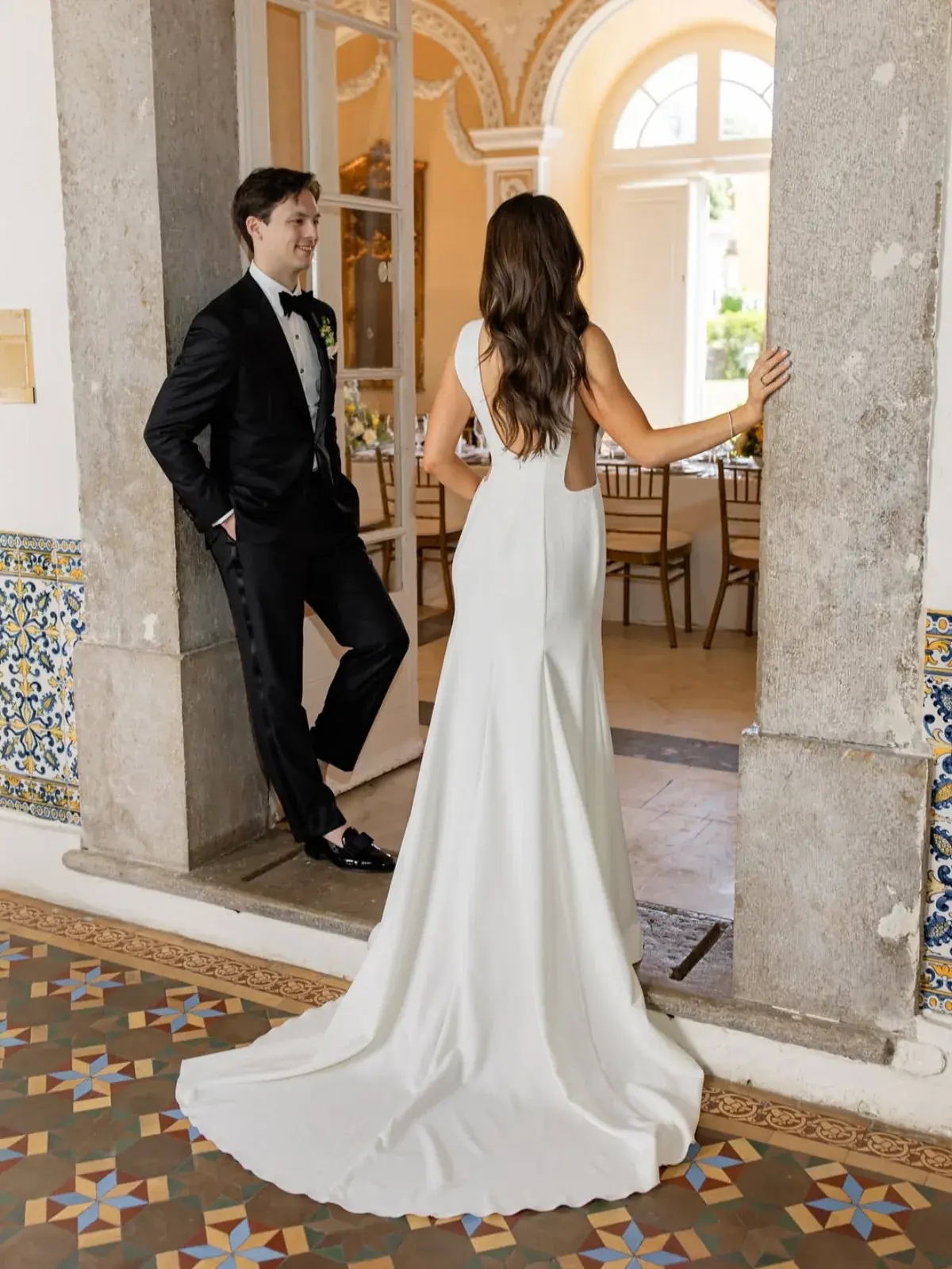 Bride and groom pausing in a palace doorway with patterned tile floor, dinner tables set beyond