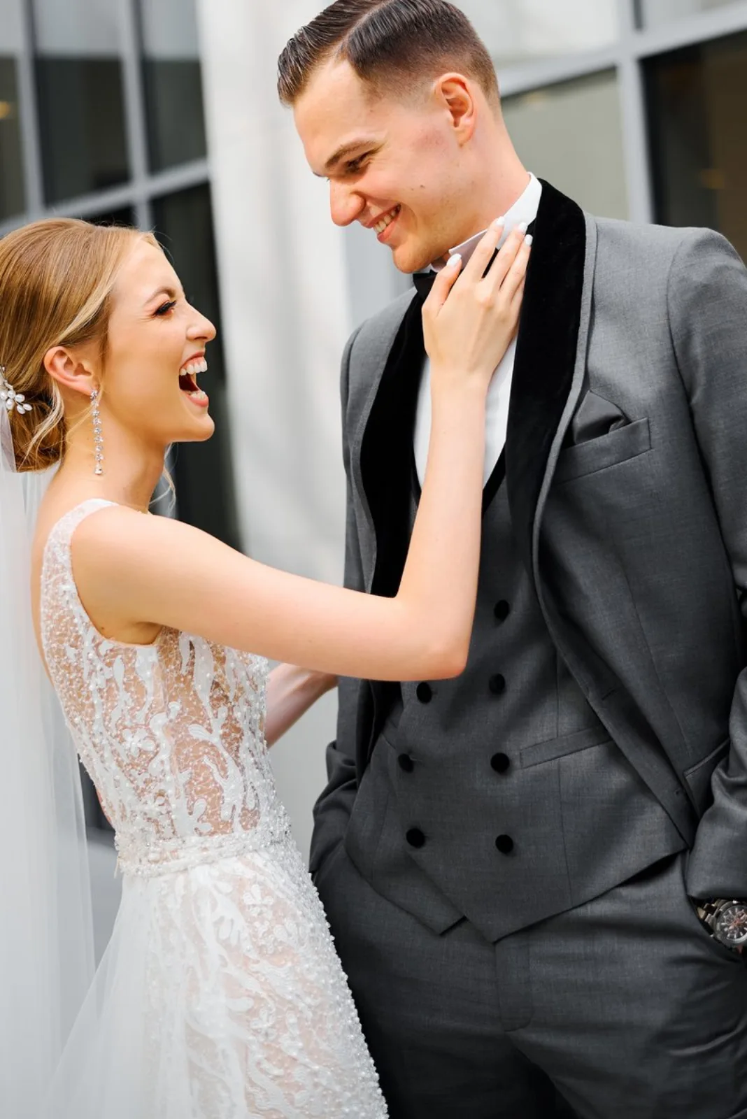 Bride laughing with the groom in his velvet-lapelled grey tuxedo outside the hotel