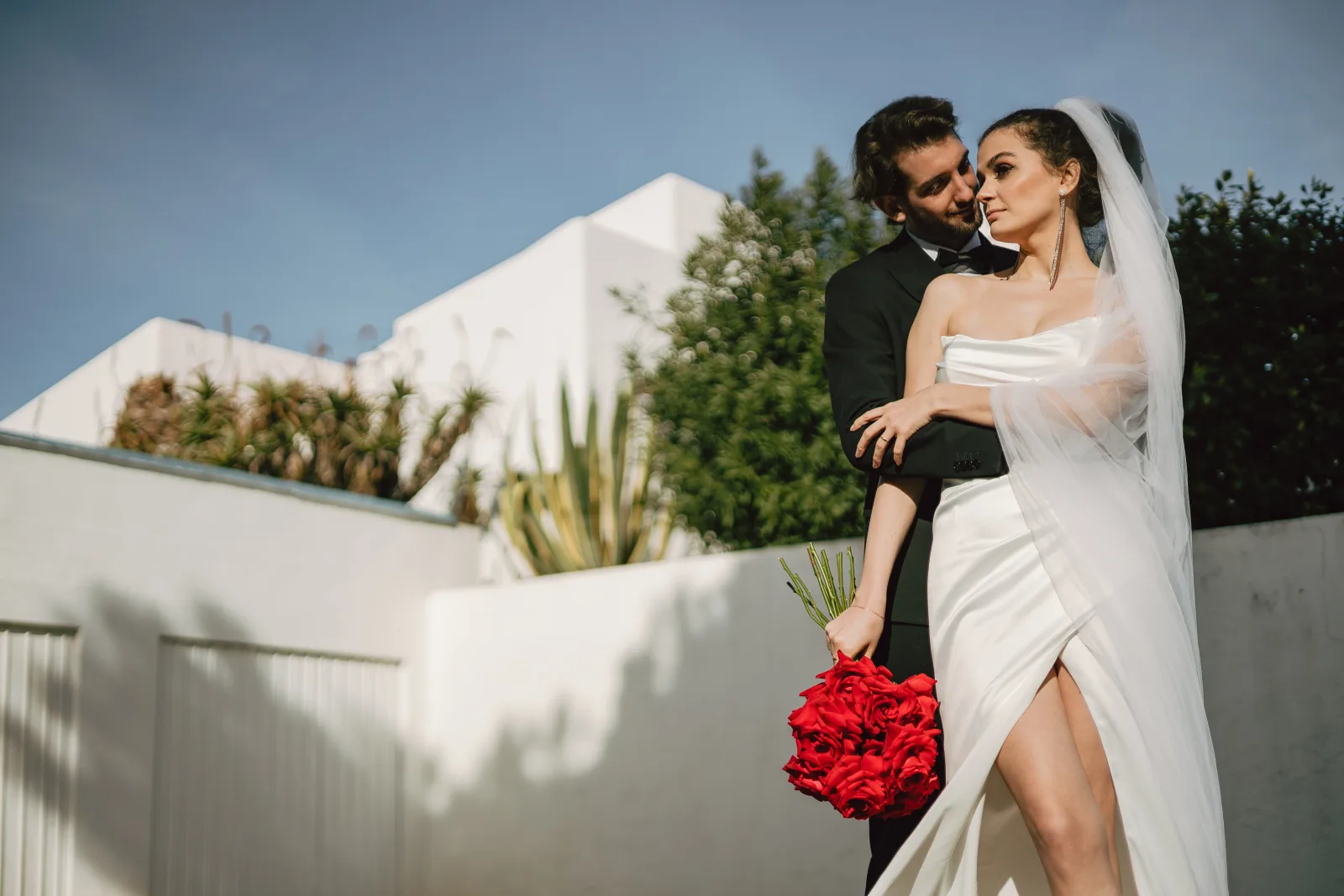 Couple embracing on a white rooftop terrace in the Algarve, red roses vivid against the render