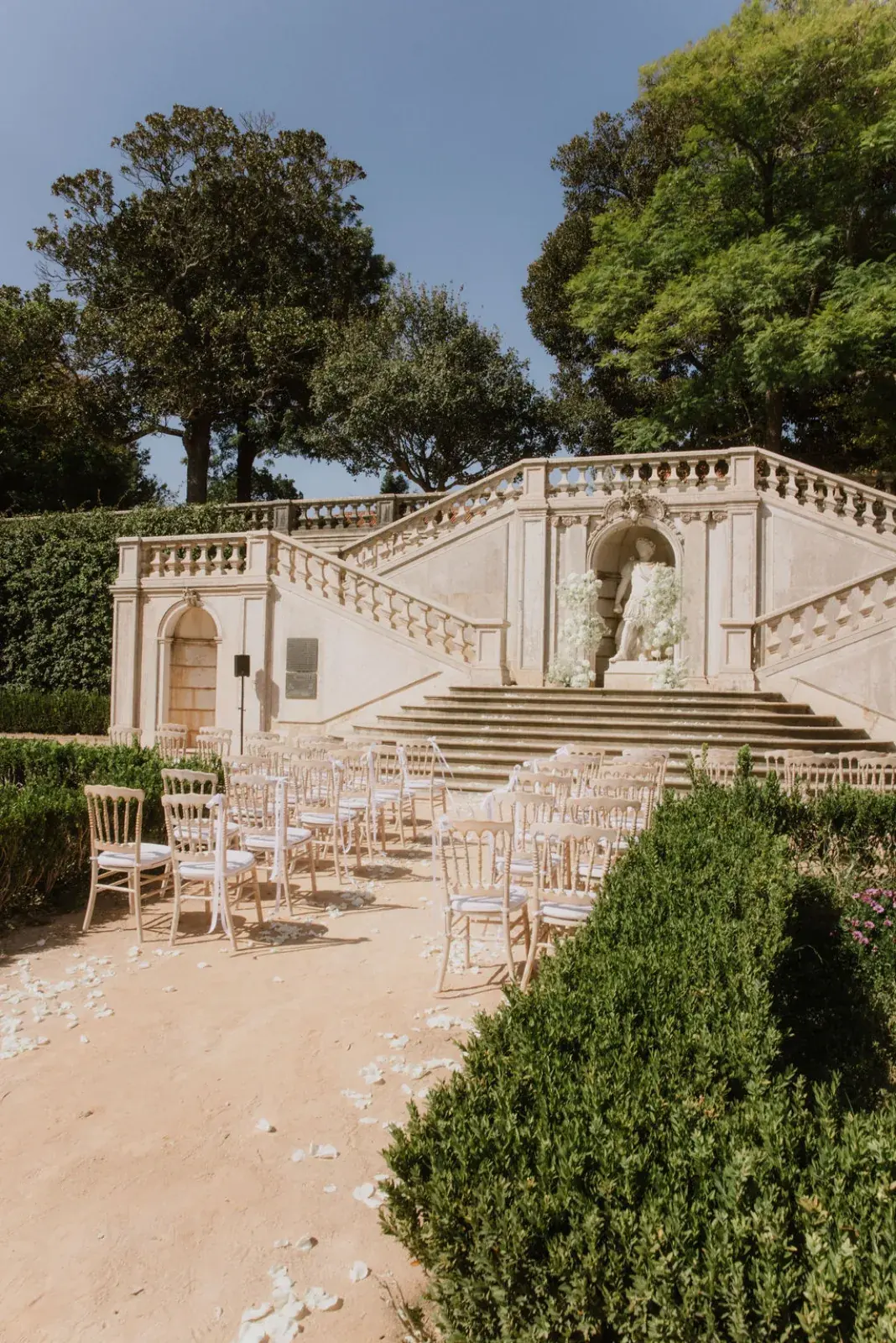 Ceremony laid out before a baroque garden staircase, white flowers marking the aisle to the statue niche