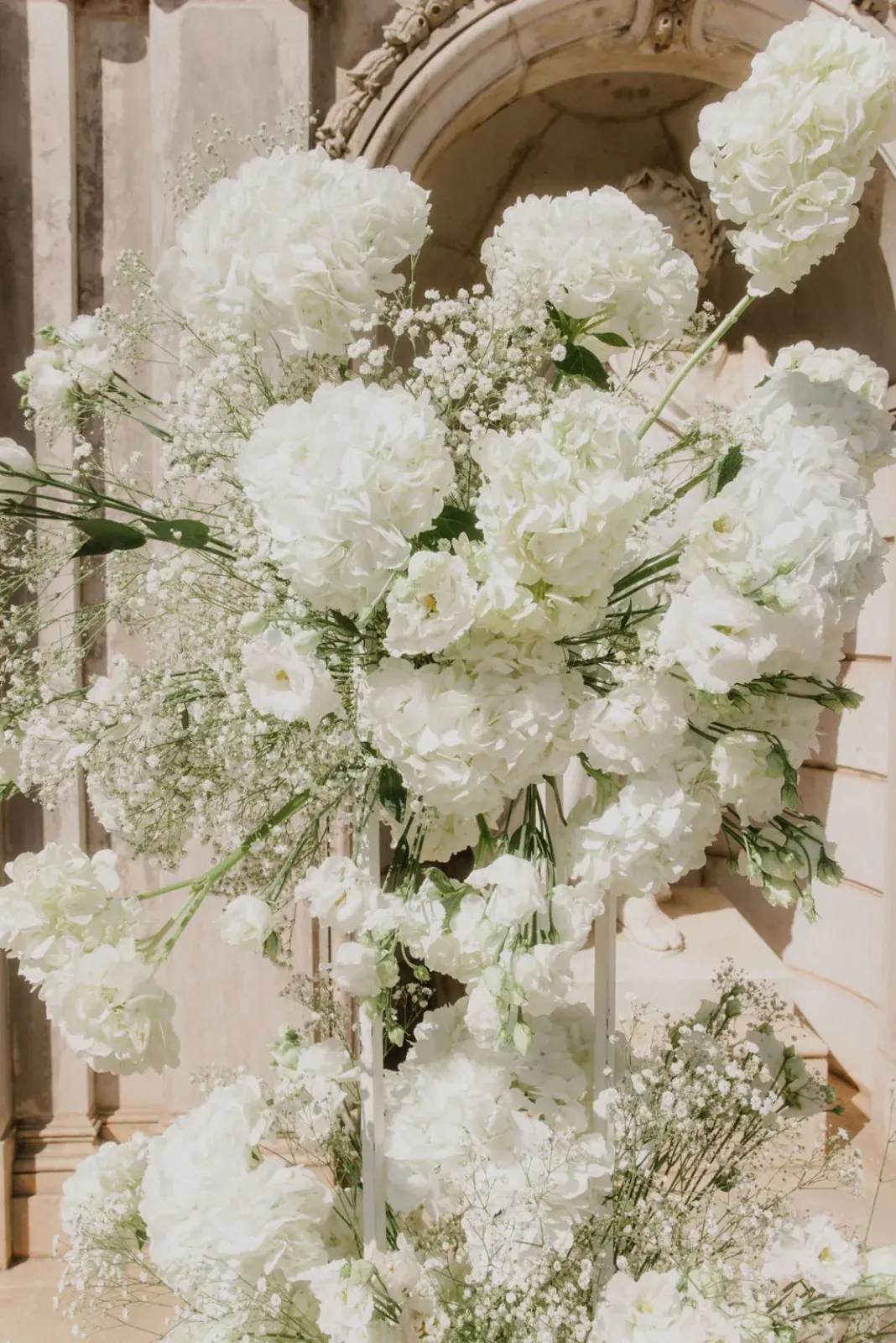 Tall arrangement of white hydrangeas and lisianthus set against a carved stone portal