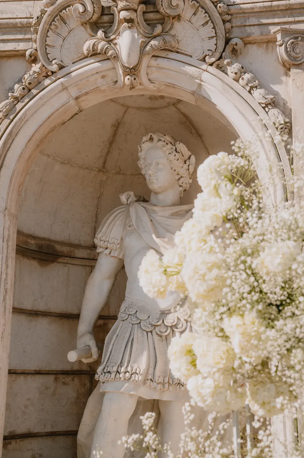 Marble statue in a stone niche beside clouds of gypsophila and white hydrangea
