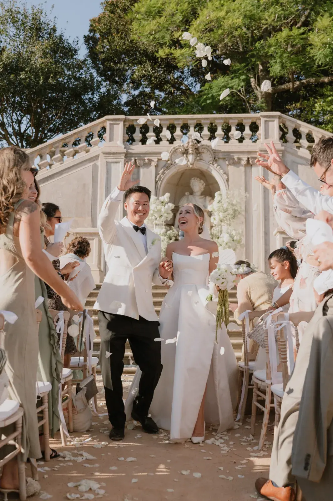 Guests throwing petals as the couple passes the garden staircase, laughter mid-step