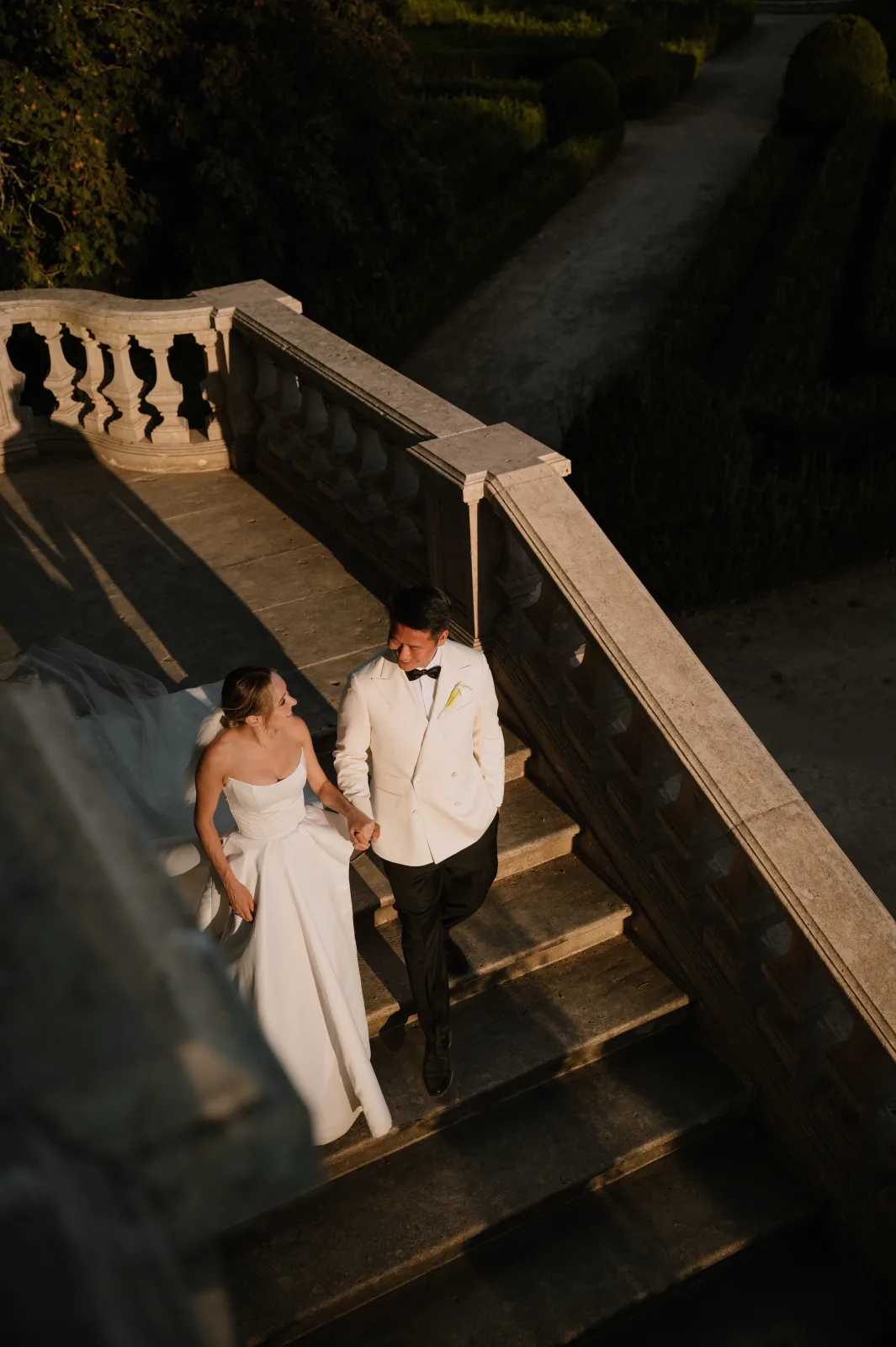 Bride and groom descending a balustraded palace staircase at dusk, warm evening light on the stone