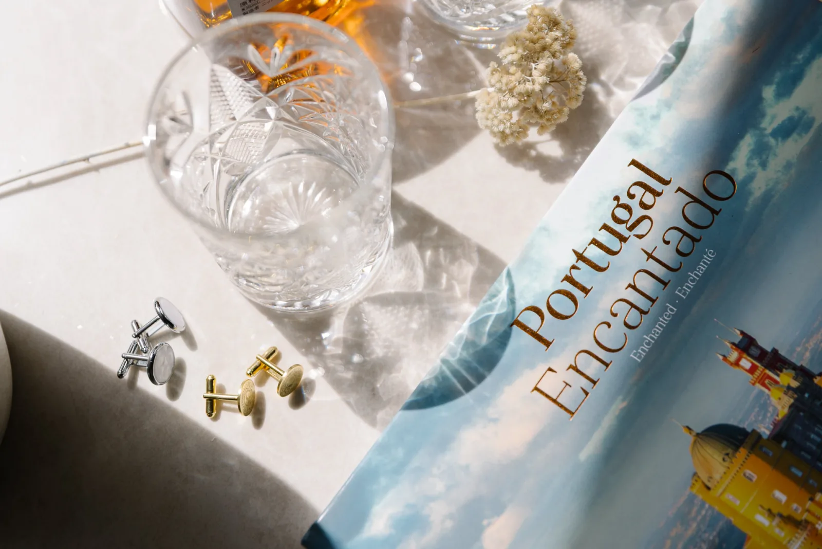Cufflinks and a cut-crystal glass beside a Portugal photography book in morning sun