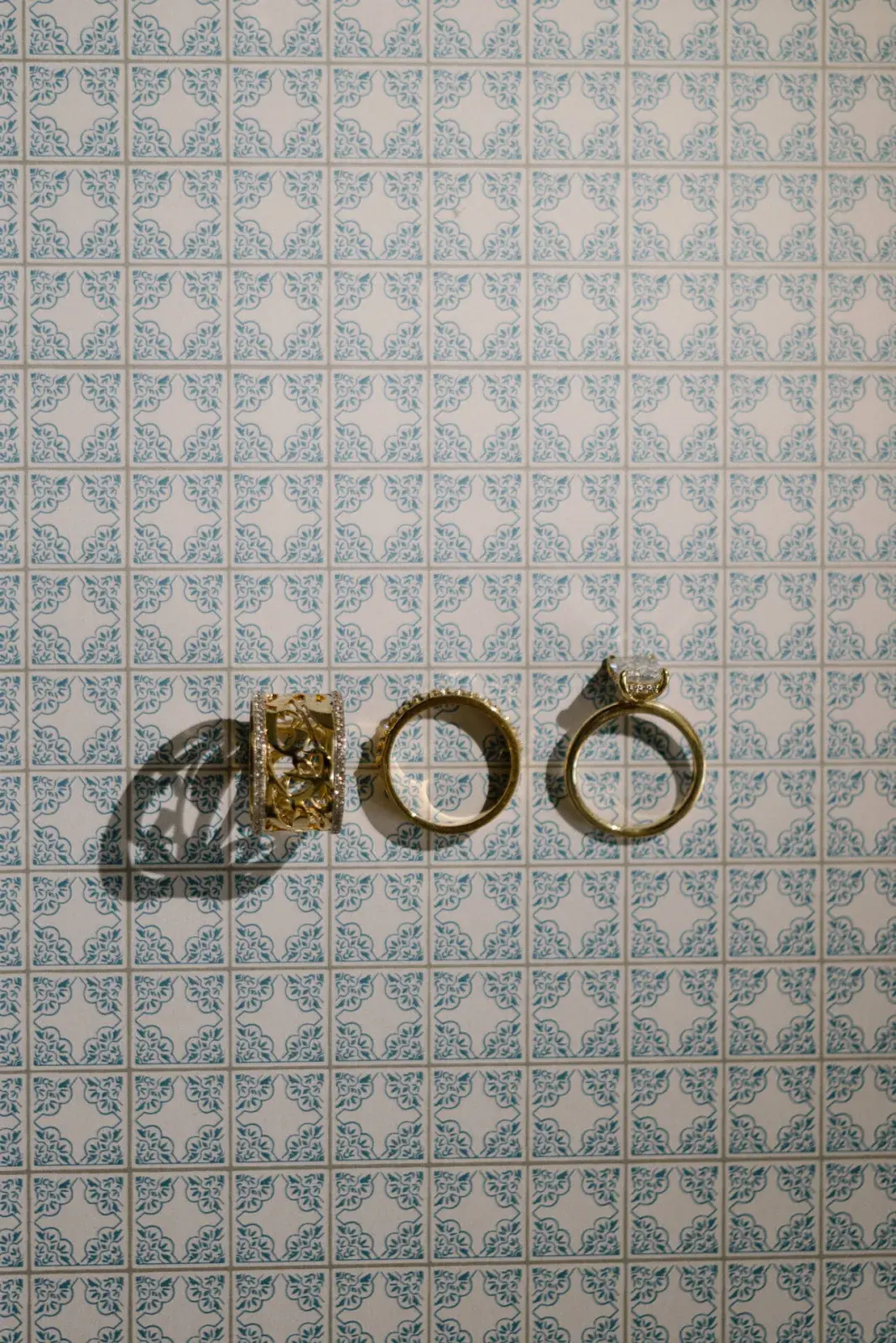 Wedding rings and gold jewellery laid on blue-and-white patterned tiles