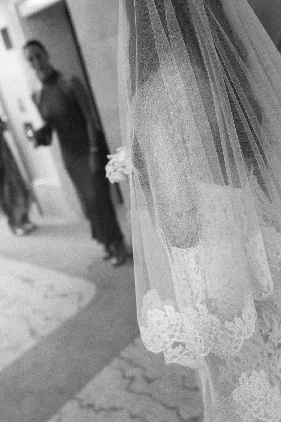 Lace-edged veil falling over the bride's gown in a palace corridor, in black and white