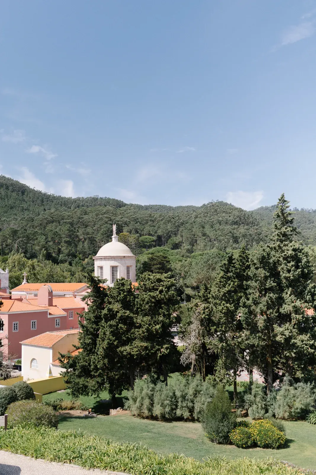 View across the palace gardens to red-tiled roofs and a domed tower against wooded hills