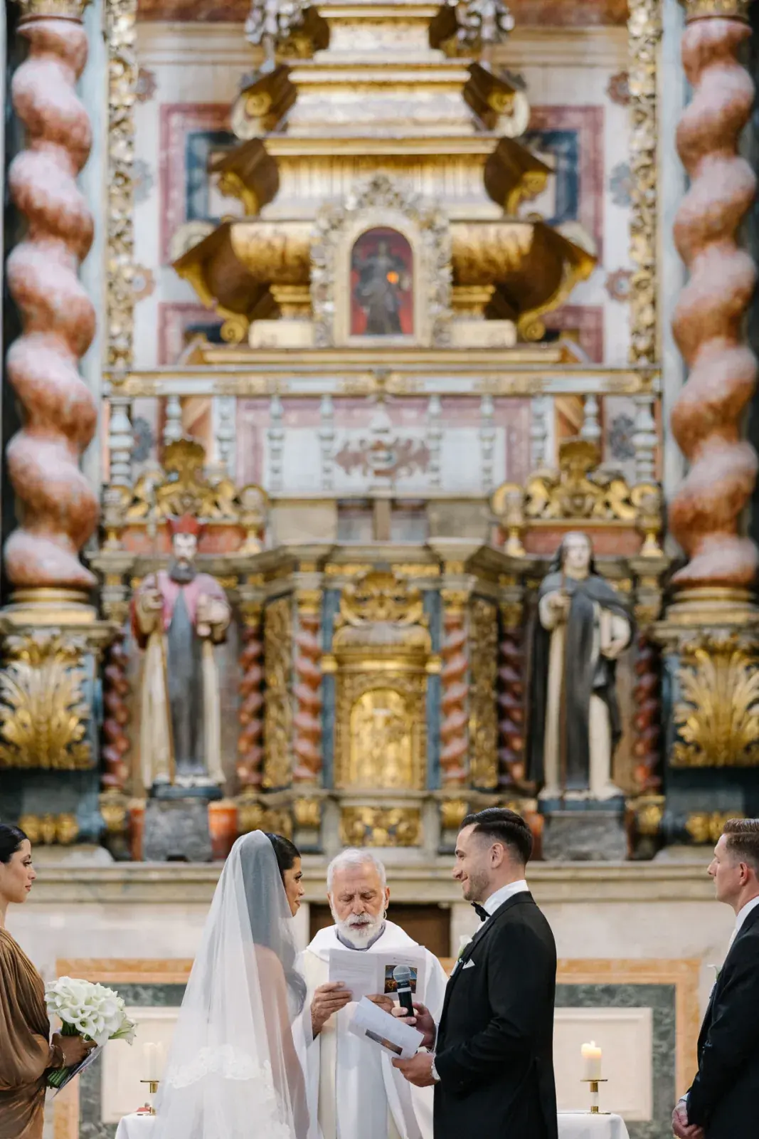 Ceremony before a gilded baroque altarpiece with barley-twist columns, the priest reading