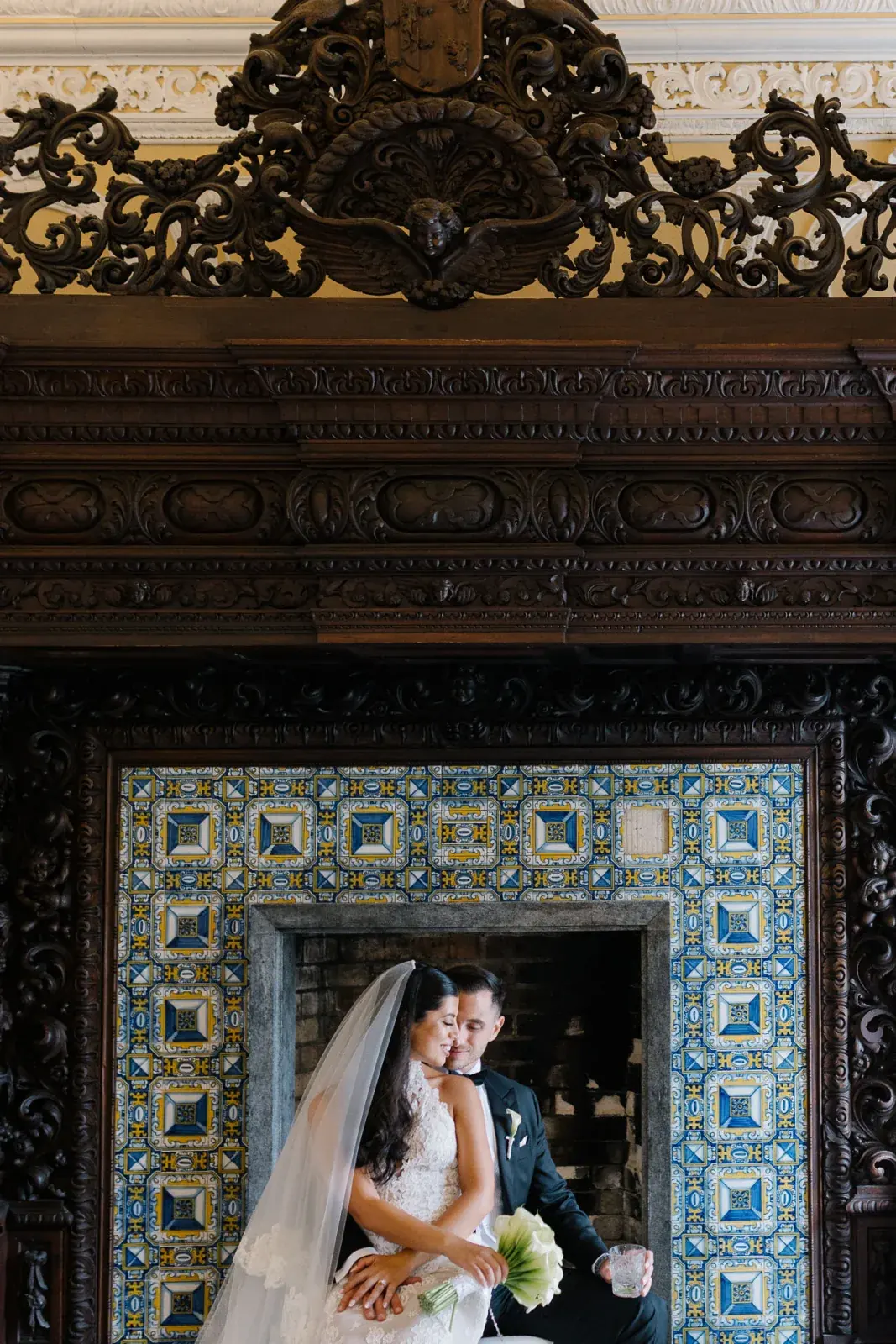 Couple seated within a carved chimneypiece lined with blue and yellow azulejos in a palace hall